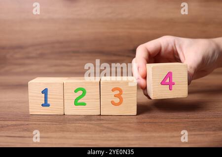 Uomo che mette il cubo con la cifra 4 a fila di altri numeri su un tavolo di legno, primo piano. Concetto passo-passo Foto Stock
