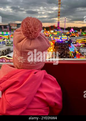 Una ragazza con un cappello rosa guarda un parco divertimenti da una ruota panoramica. Foto di alta qualità Foto Stock