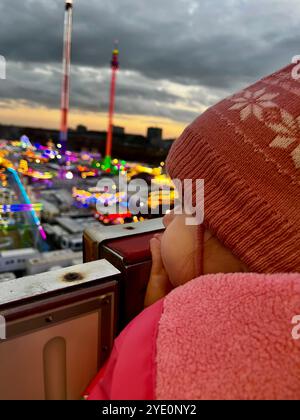 Una ragazza con un cappello rosa guarda un parco divertimenti da una ruota panoramica. Foto di alta qualità Foto Stock