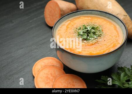 Deliziosa zuppa di patate dolci con parmigiano nel recipiente e ingredienti freschi sul tavolo grigio, primo piano Foto Stock