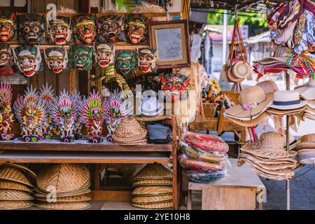 Maschere, statue e cappelli di paglia colorate in legno sono esposti su scaffali e scaffali in un negozio di souvenir balinese, creando uno shoppin vivace e culturale Foto Stock