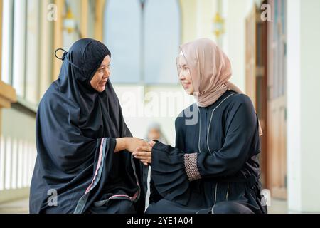 Due belle donne musulmane asiatiche, ciao, saluto, e Corano al tavolo di legno a casa sua durante la notte durante il mese del ramadan, arabo Foto Stock