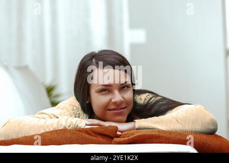 La giovane donna poggia la testa su un comodo cuscino, trasudando un senso di calma e sicurezza di sé mentre si gode un momento di tranquillo relax in lei Foto Stock