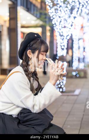 Una giovane e carina donna taiwanese di 20 anni che indossa abiti in bianco e nero, seduta e riposante di notte in mezzo a splendide illuminazioni in uno shopping Foto Stock