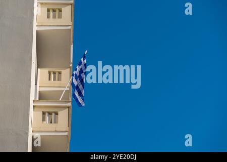 Balconi gialli e bandiera greca contro il cielo azzurro: Un omaggio alle festività statali Foto Stock