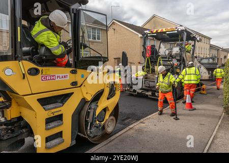 Un team di operai che gestiscono macchinari pesanti per ripavimentare una strada residenziale nel Wiltshire. Foto Stock