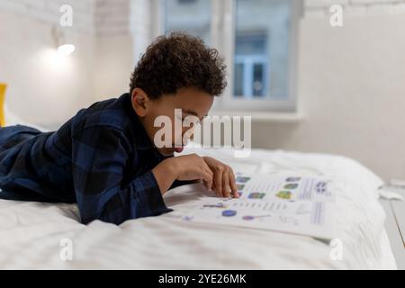 Ragazzo afroamericano dai capelli ricci sdraiato sul letto con un libro e sembra eccitato Foto Stock