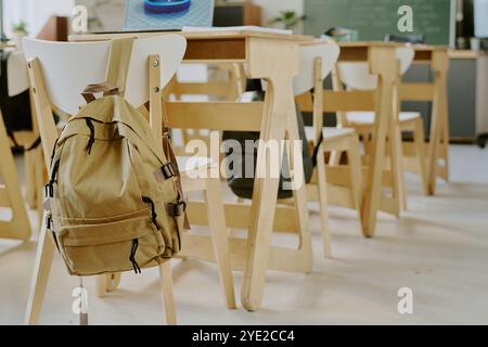 Interno dell'aula con sedie e scrivanie vuote, con zaino sul retro di una sedia, che suggerisce l'assenza di studenti o la lezione in corso Foto Stock