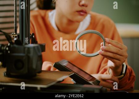 Persona che osserva con attenzione il processo di stampa 3D mentre tiene l'oggetto stampato IN un ambiente di officina dettaglio messa a fuoco e precisione coinvolte nella moderna tecnica di fabbricazione Foto Stock