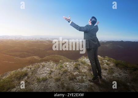 Vista posteriore dell'uomo d'affari in piedi mentre guarda la vista sulle montagne con braccio rialzato sulla cima della valle. Concetto di business, successo e motivazione Foto Stock