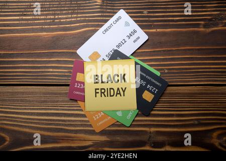 Vista dall'alto delle note con testo del Black Friday su una pila di carte di debito o di credito su sfondo in legno. Le carte sono di colori diversi. Modello o modello. Foto Stock