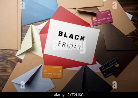 Vista dall'alto della busta rossa e cartolina con cartolina bianca con scritta Black Friday su una pila di busta e carta di credito su sfondo in legno. Foto Stock