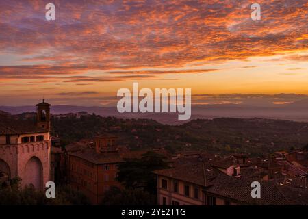 Splendido cielo all'alba con nuvole arancioni sopra la città vecchia di Perugia, con campanile medievale e campagna umbra sullo sfondo Foto Stock