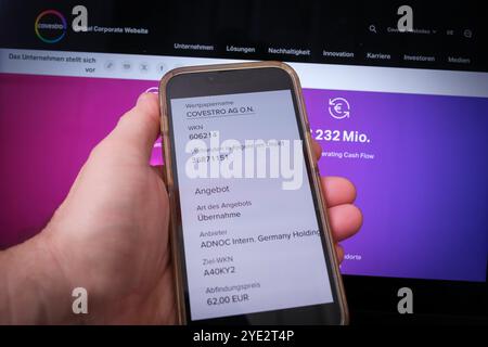 Covestro: Tenere a mano il cellulare che mostra l'offerta di acquisto di ADNOC Foto Stock