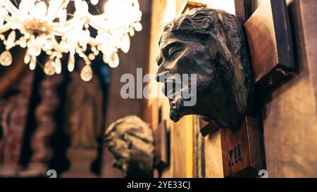 Le intricate sculture intagliate della testa adornano le pareti di un edificio storico ad Alba, Italia, illuminato da uno splendido lampadario Foto Stock