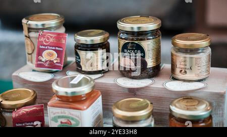 Un vivace assortimento di vasi artigianali pieni di condimenti gourmet è esposto in un mercato di Alba, Italia, che mette in evidenza le delizie culinarie locali Foto Stock