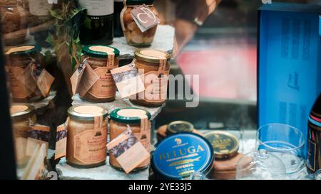 Diversi vasetti ripieni di crema artigianale di nocciole sono ordinatamente disposti su uno scaffale in un negozio ad Alba, Italia. L'ambiente mette in mostra prelibatezze locali in una Foto Stock