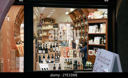 I visitatori esplorano un'affascinante enoteca ad Alba, in Italia, circondata da scaffali pieni di una vasta gamma di vini locali e prodotti gastronomici gourmet, creando un del Foto Stock