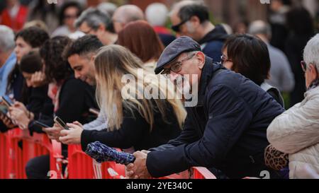 Ad Alba, in Italia, un gruppo di partecipanti diversificato attende con ansia un evento. Molti sono impegnati con i loro telefoni mentre si godono il vivace ambiente Foto Stock