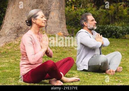 Meditando all'aperto, coppia matura seduta a gambe incrociate in un momento di pace Foto Stock