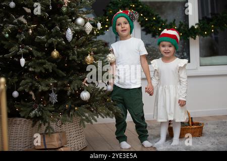 Carini figli fratello e sorella a Natale. Un ragazzo e una ragazza con i cappelli di Babbo Natale aspettano i regali di Natale a casa. Foto Stock