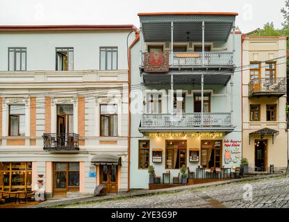 Una tipica strada laterale acciottolata di Tbilisi con piccoli ristoranti e case in legno intagliato con balconi Foto Stock