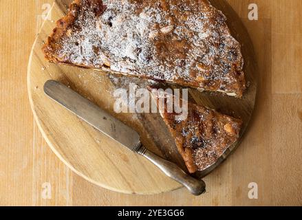 Fotografia da tavolo di un tradizionale panforte da dessert italiano a fette su un tagliere di legno con un coltello antico Foto Stock