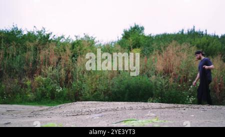 Un uomo solitario cammina lungo uno stretto sentiero sterrato circondato da fitte piante verdi. Ideale per avventure, escursioni e video naturalistici. Foto Stock