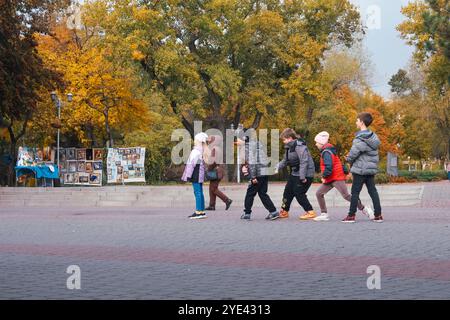 Un vivace gruppo di bambini che camminano insieme gioiosamente in un bellissimo parco, circondato da una serie di vibranti foglie autunnali, creando una deliziosa scena piena di divertimento all'aperto ed esplorazione Foto Stock