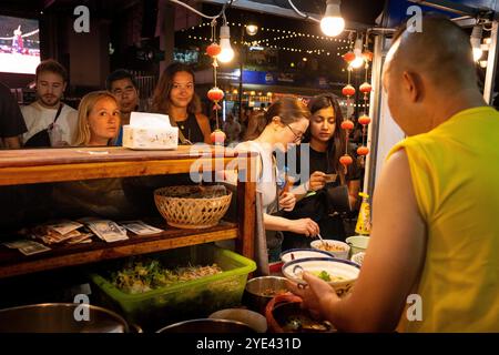 Clienti stranieri che acquistano spaghetti da un venditore al mercato notturno di Luang Prabang. Foto Stock