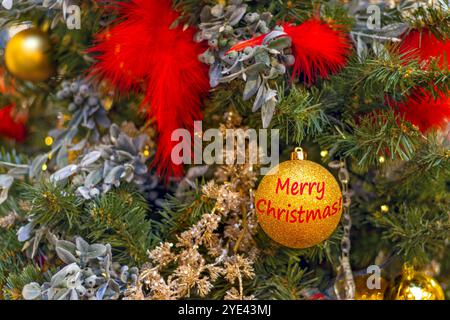 Albero di Natale decorato con piume rosso brillante e palle d'oro. Iscrizione su ballo di buon Natale. Copia spazio Foto Stock
