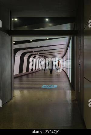 Londra, Inghilterra - 18 ottobre 2023 - turisti e pendolari che camminano lungo il futuristico tunnel pedonale con illuminazione a LED integrata Foto Stock