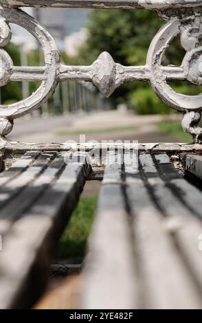 Primo piano della panca da giardino in stile vittoriano in ghisa dipinta di bianco nel parco cittadino. Luce solare sulla superficie dello schienale di un banco in ghisa antica decorata vuota in Foto Stock