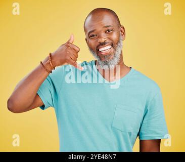 Uomo maturo, ritratto e nero con gesti telefonici per chiamarmi, appendi il cartello o Shaka su uno sfondo giallo dello studio. Africano, uomo o felice Foto Stock