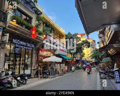 Hanoi, Vietnam: Vita quotidiana, traffico e skyline nelle strade affollate del centro della capitale, con auto e moto che passano a tutta velocità Foto Stock