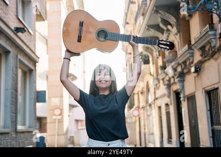 ritratto di una giovane donna latina che solleva una chitarra classica sopra la testa Foto Stock