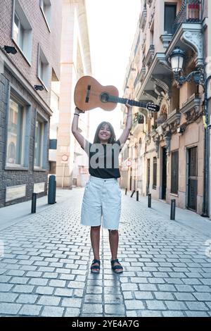 vista completa di una giovane donna latina che solleva una chitarra classica sopra la testa Foto Stock