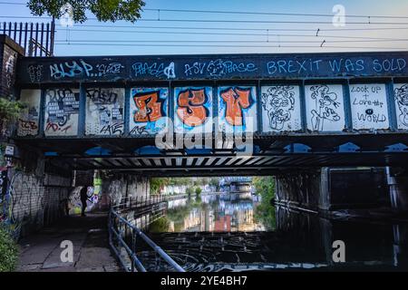 Murales e graffiti vicino a un ponte ferroviario lungo il canale di Regent, Camden, Londra Foto Stock