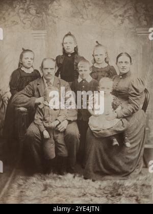 Inghilterra. Circa.1895 – Una fotografia formale di uno studio di una famiglia britannica del tardo Vittoriano. Raffigurati un marito e una moglie con i loro sei figli. La madre e le bambine indossano abiti con maniche di maniche di montone e i ragazzi, giacche Norfolk. Foto Stock