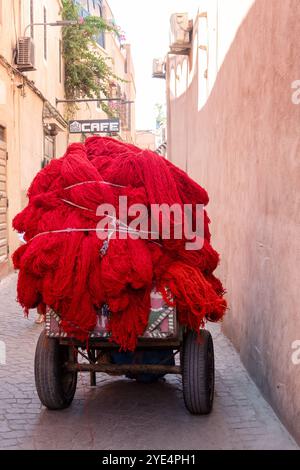 Marrakech, Marocco. Un carrello a mano carico di lana tinta rossa viene trasportato attraverso i suk centrali nella medina di Marrakech o nella città vecchia Foto Stock
