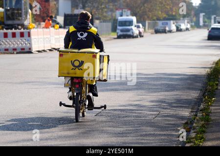 Augusta, Baviera, Germania - 29 ottobre 2024: Corriere di lettere Deutsche Post che consegna lettere in bicicletta in città *** Postbote der Deutschen Post bei der Briefzustellung auf dem Fahrrad in der Stadt Foto Stock