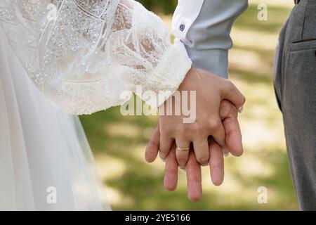 Intimo momento di una sposa e di uno sposo che si tengono per mano in un lussureggiante ambiente all'aperto. Foto Stock