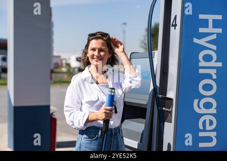 Donna tiene un ugello di alimentazione dell'idrogeno su una stazione di rifornimento dell'idrogeno. Rifornimento di carburante per auto con idrogeno. Foto Stock