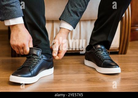Uomo elegante che si adatta ai pantaloni indossando le sneaker nere. Foto Stock