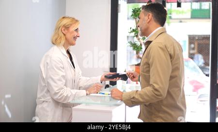 Un medico con un cappotto bianco consegna un terminale di pagamento a un paziente alla reception di una clinica di bellezza. Il paziente sta pagando il trattamento Foto Stock