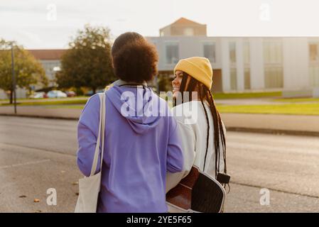 Questa immagine cattura due giovani studenti latini che condividono un momento di gioia mentre camminano in una strada soleggiata del campus, riflettendo la vita spensierata dell'università e. Foto Stock