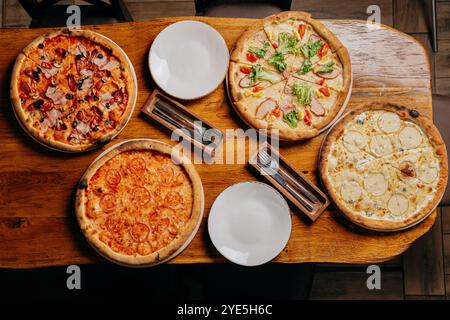 Pizze assortite su un tavolo rustico in legno, pronte da servire con piatti e posate Foto Stock