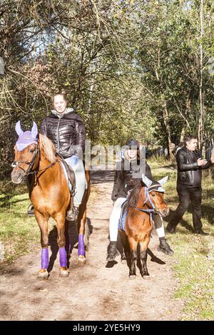 Due amiche, una più grande e una più giovane, una a cavallo, una a cavallo, una a cavallo nel vicolo in una soleggiata giornata autunnale, come Don Chisciotte e Sancho Panza. Foto Stock