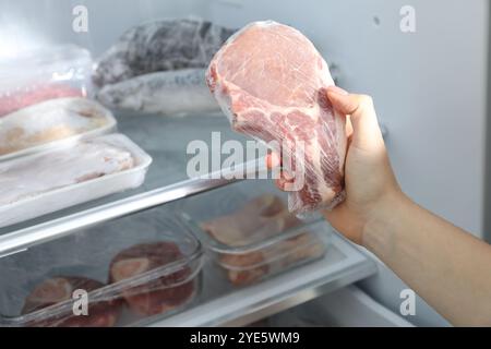 Donna che prende una bistecca di maiale congelata dal frigo, primo piano Foto Stock