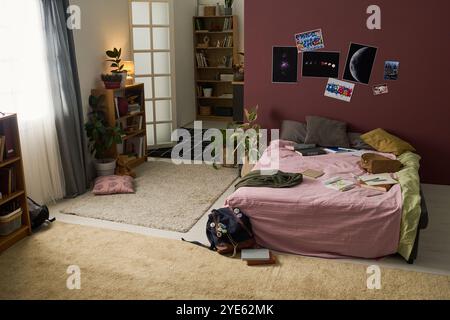 Camera ben illuminata con biancheria da letto rosa e decorazioni verdi con libri e computer portatile sul letto, comoda e funzionale zona giorno adatta al relax e al lavoro Foto Stock